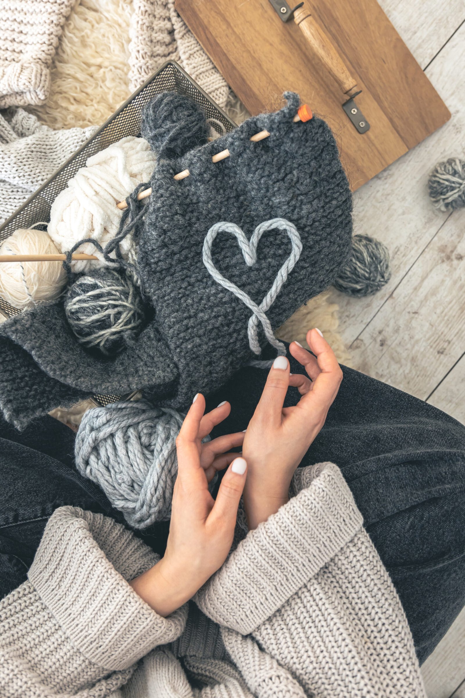 A woman with gray threads and a knitted element sits on the floor, top view. Handmade clothes. The girl goes in for her hobbies. Love knitting concept.